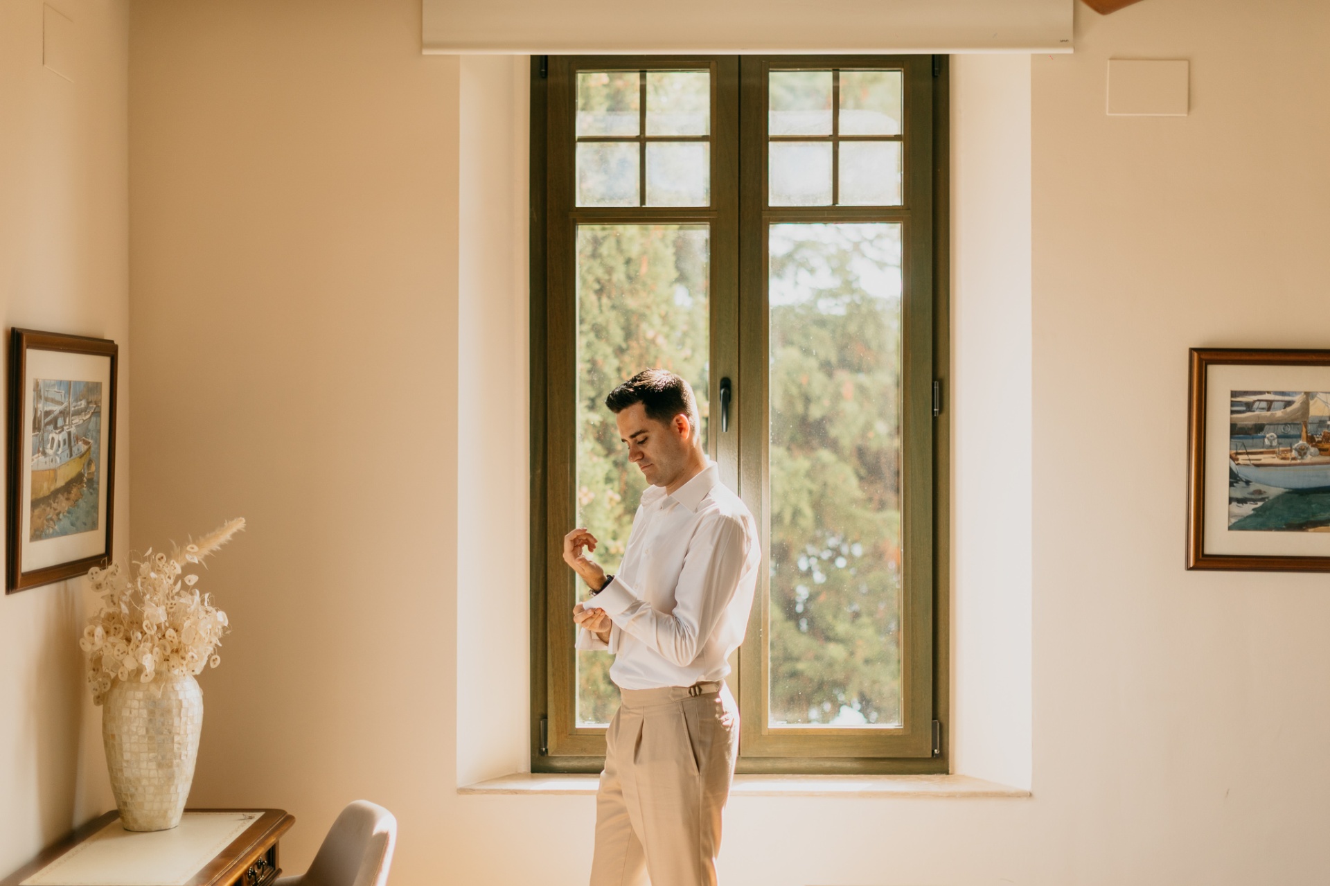 Cameron adjusting his cufflinks by a window at Xalet del Nin with golden morning light