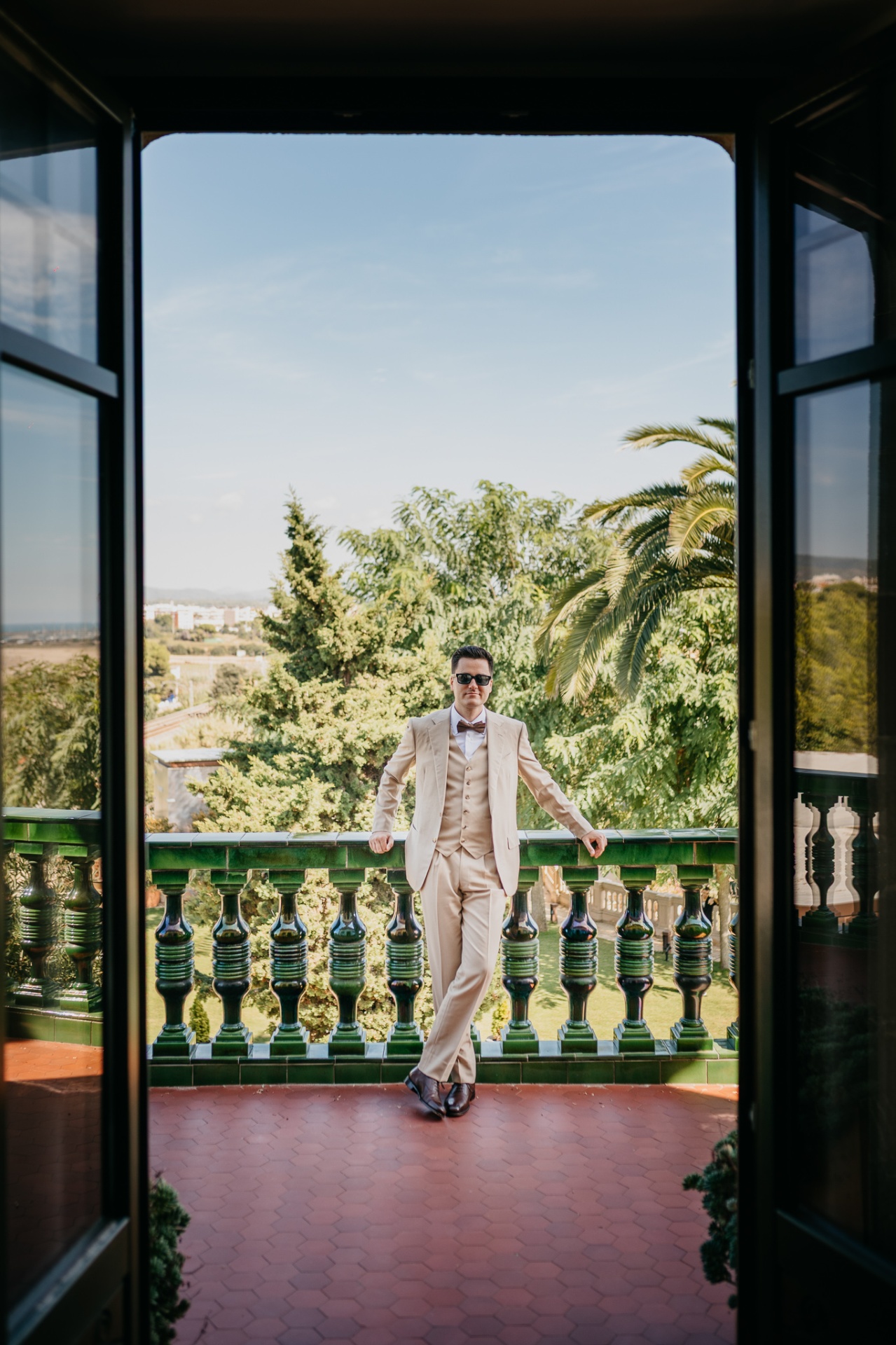 Cameron posing in a beige suit on the green-tiled balcony of Xalet del Nin with Mediterranean views
