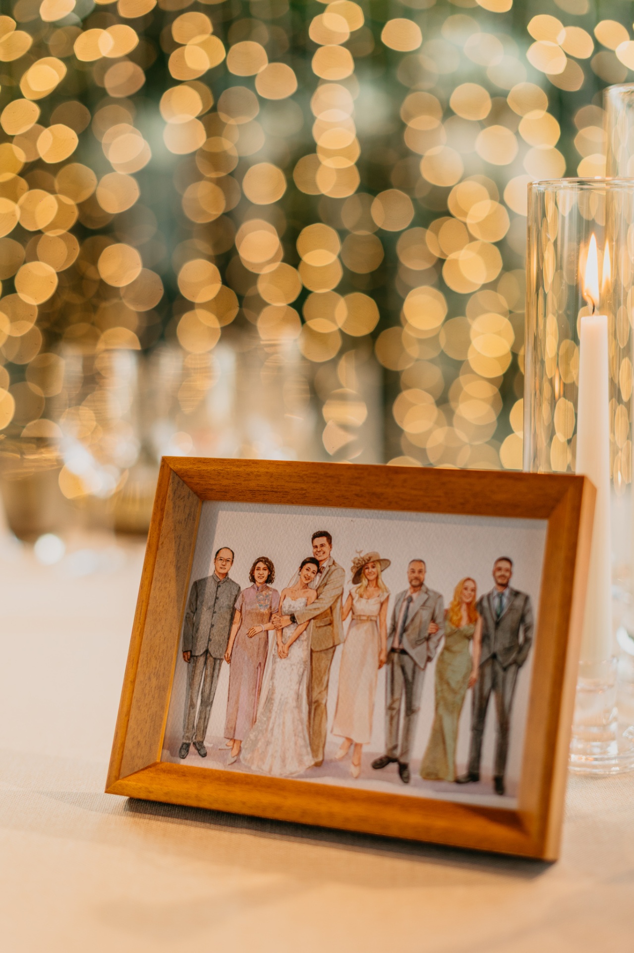 Watercolour family portrait in a wooden frame with fairy light bokeh at the reception table