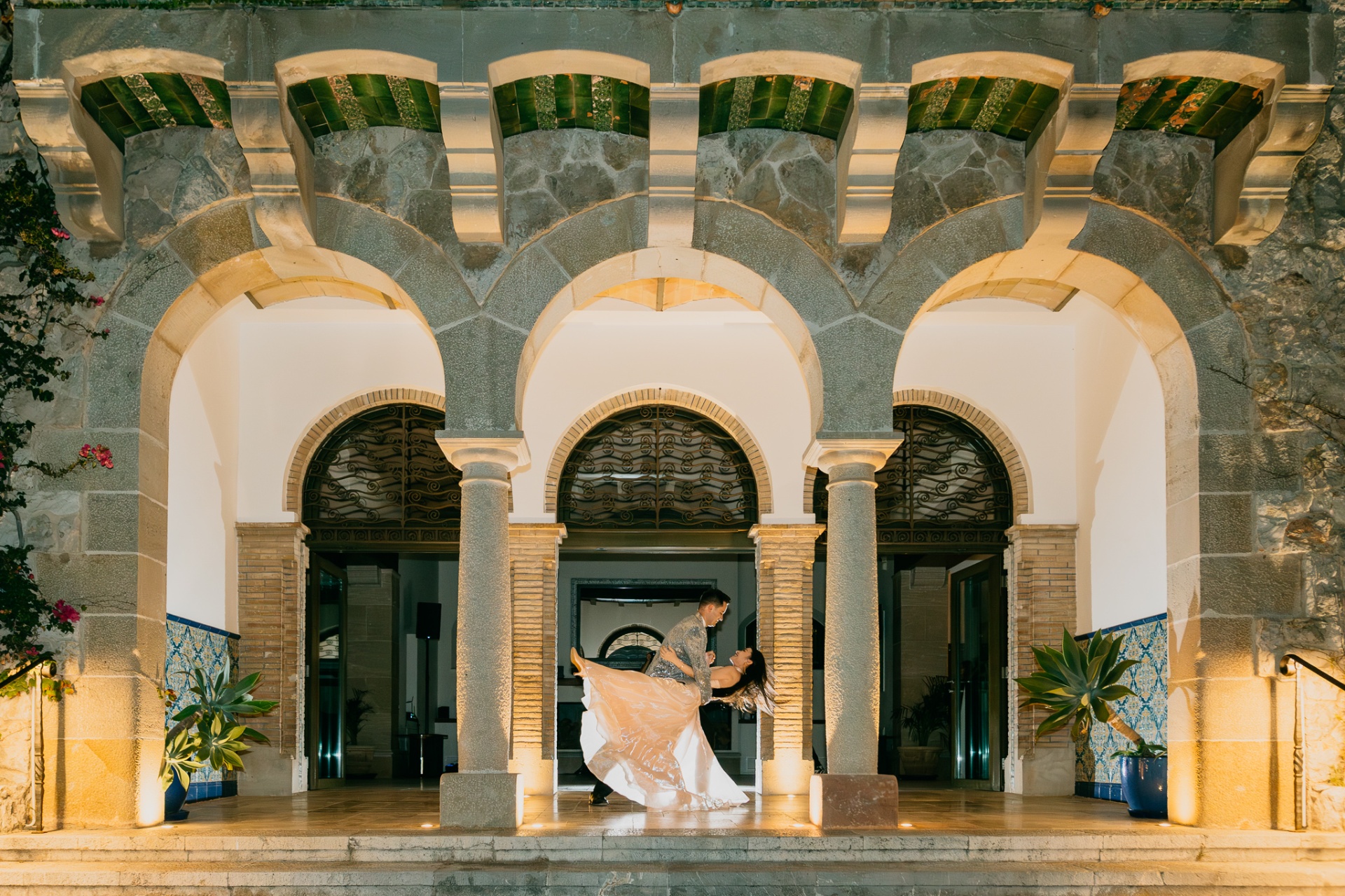 Cameron dipping Kara in a dramatic dance move under the illuminated Moorish arches of Xalet del Nin at night
