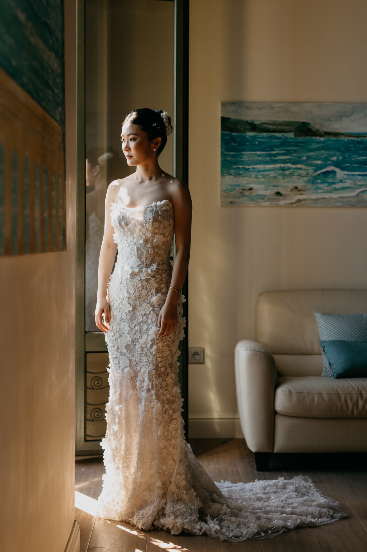 Kara in her lace wedding dress standing by a window with a seascape painting at Xalet del Nin