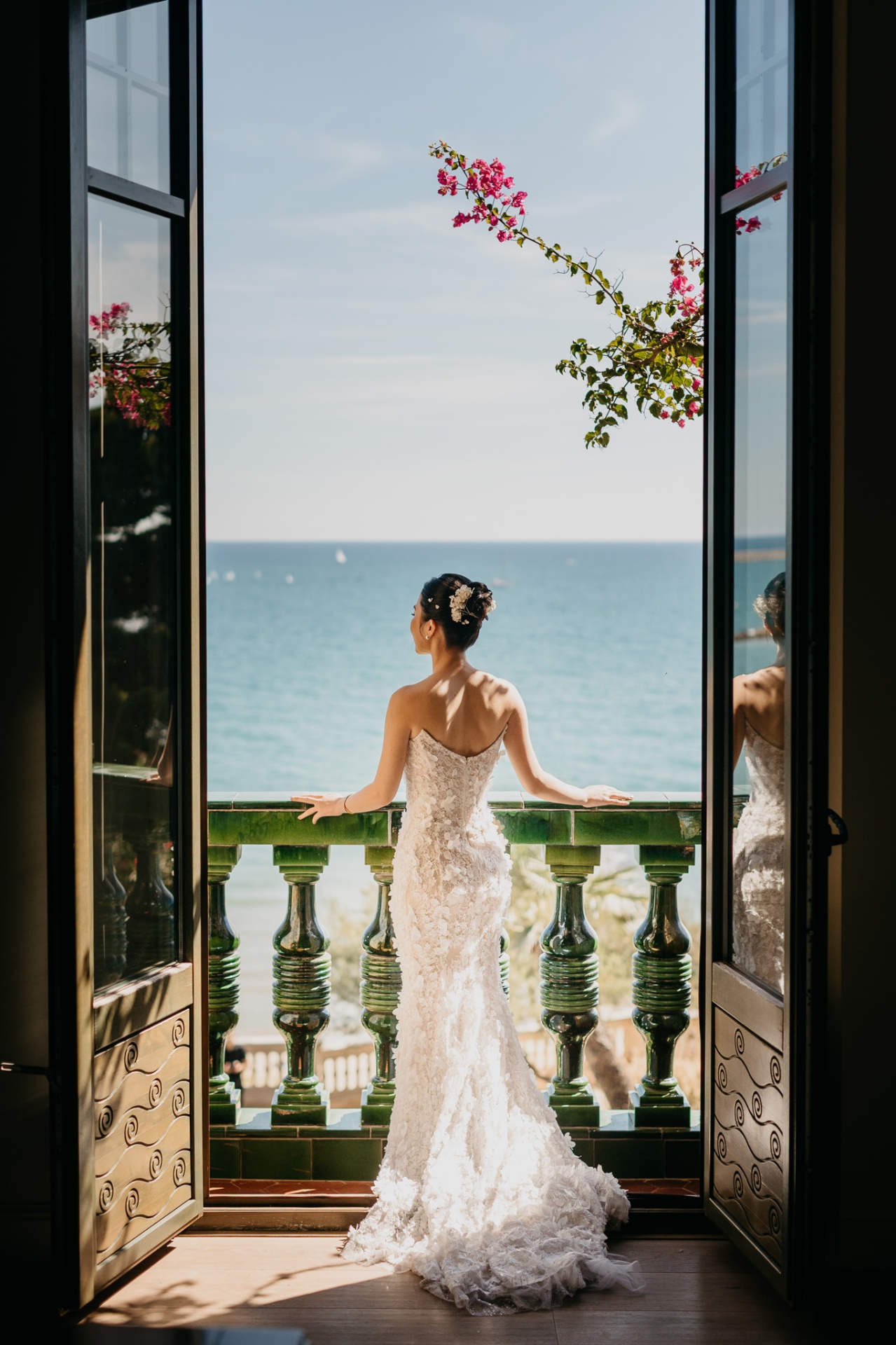 Kara looking out from the balcony of Xalet del Nin towards the Mediterranean in her bridal gown with bougainvillea