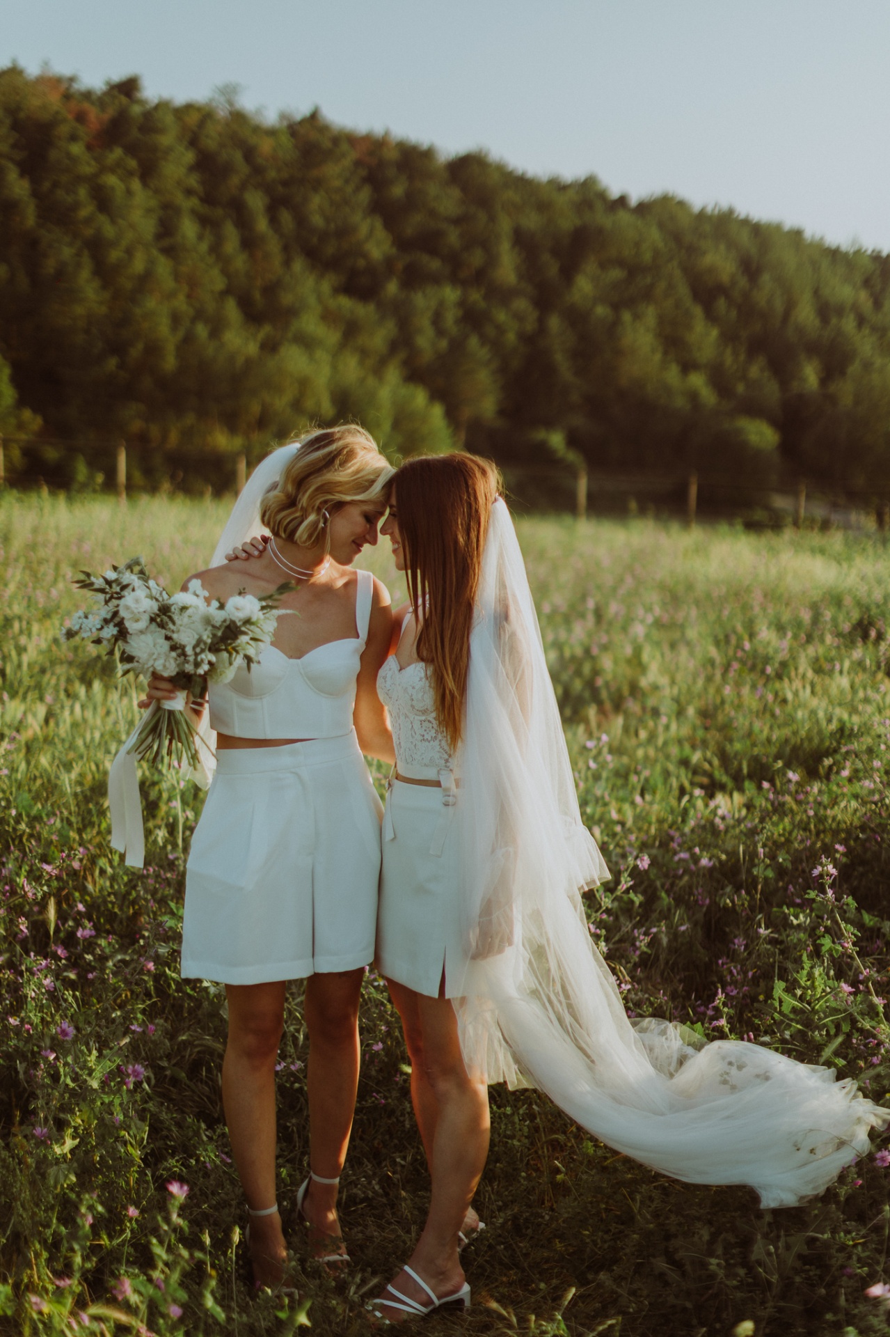Brides touching foreheads in tender moment among wildflowers