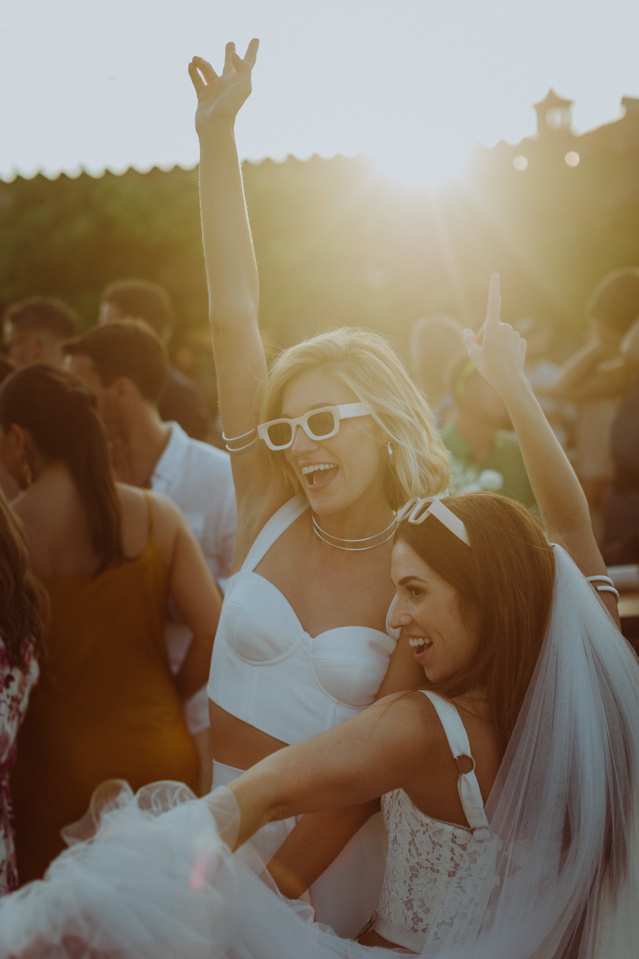 Brides dancing and celebrating with arms raised at sunset party