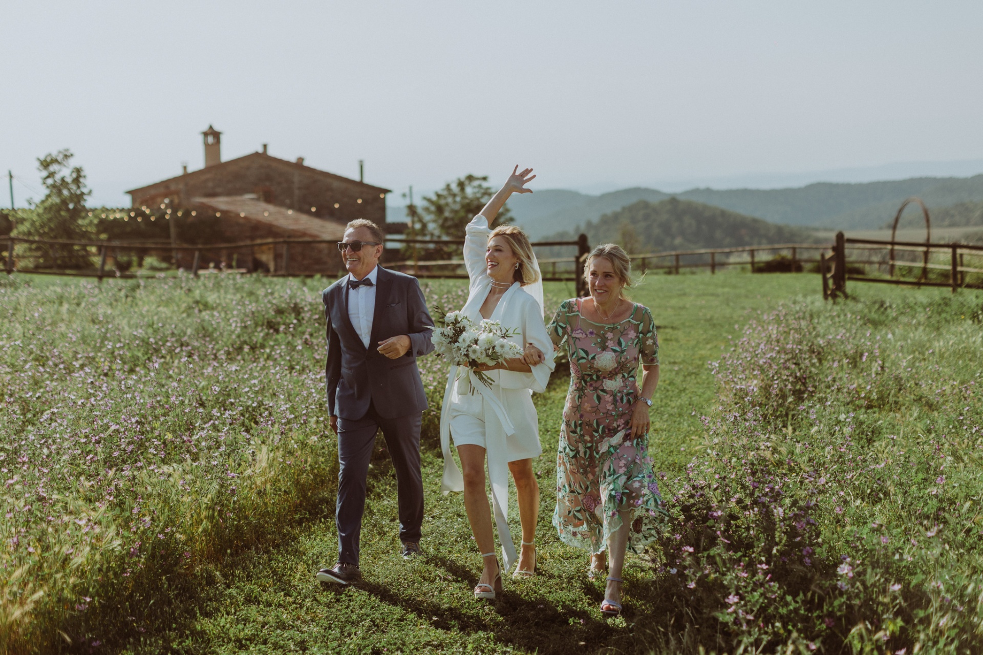 Bride walking through wildflower fields with family at This Must Be The Place