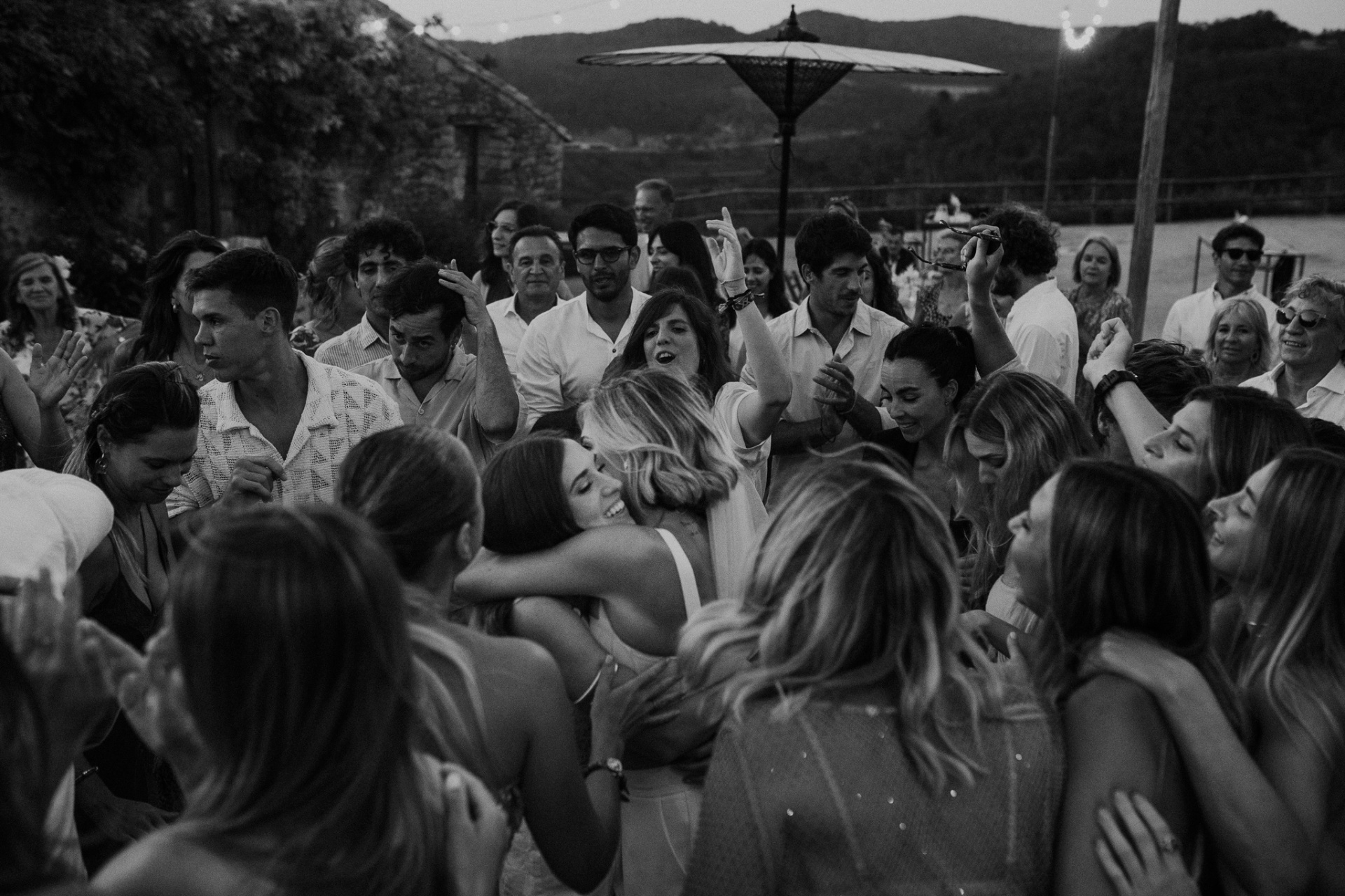 Guests surrounding brides in emotional group hug on dance floor