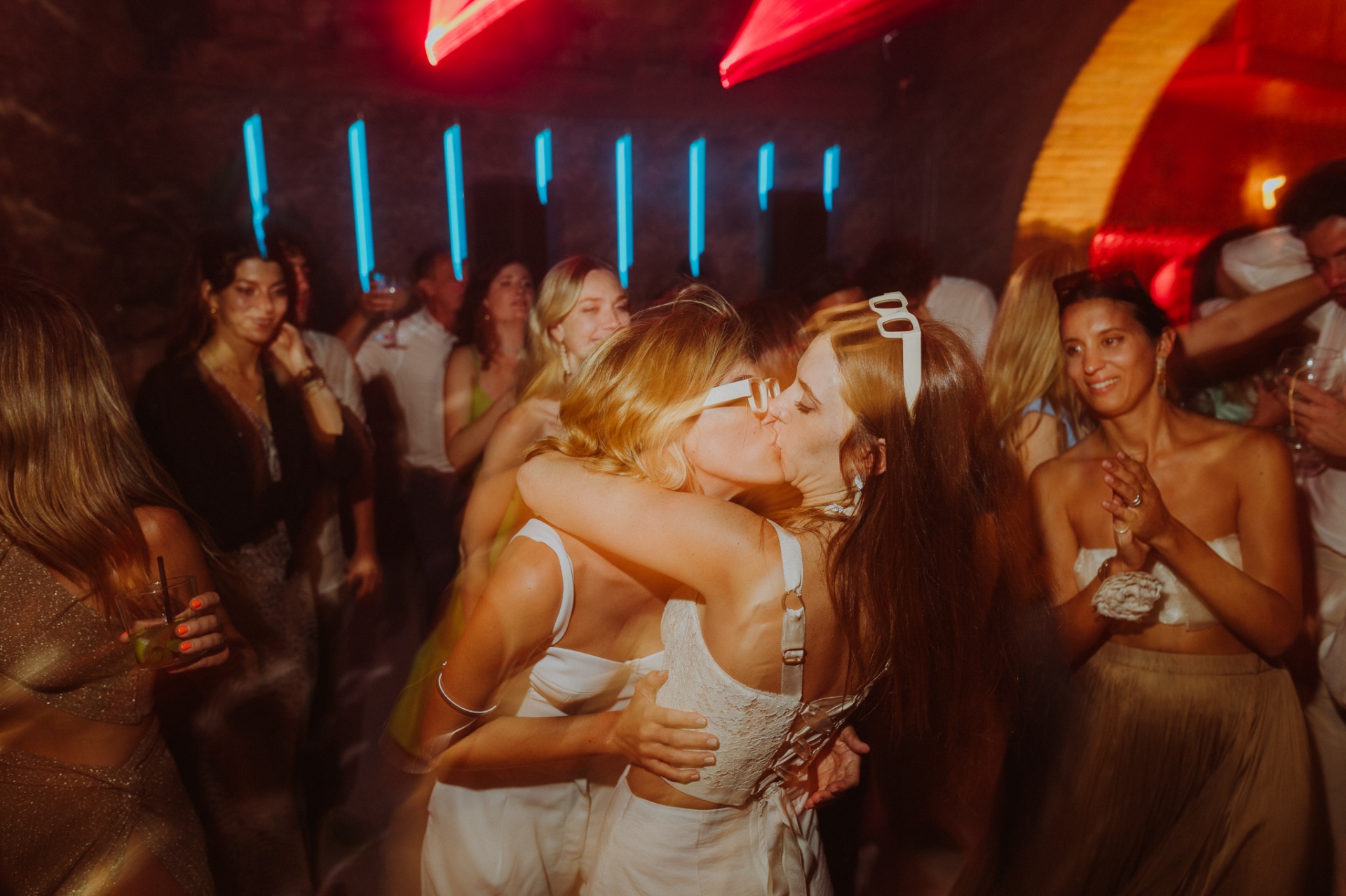 Brides kissing on dance floor under neon lights at late night party