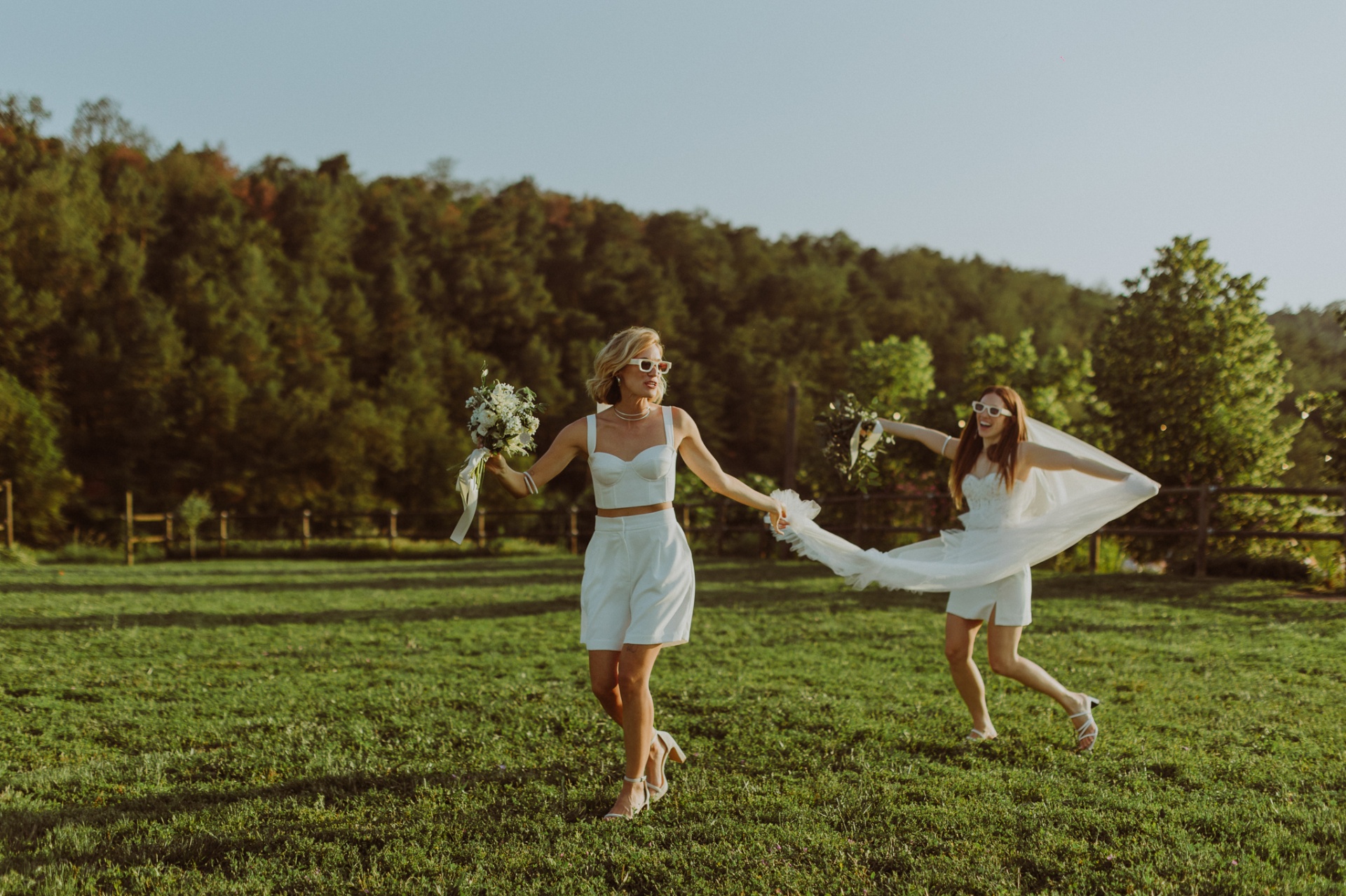 Brides running through green fields with bouquets at golden hour