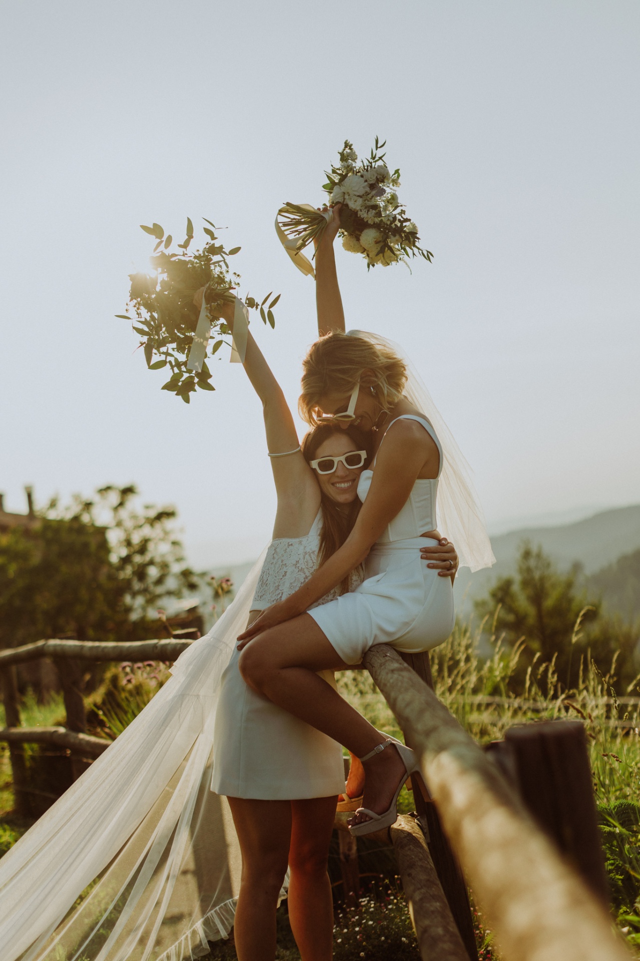 Chiara and Ro embracing with bouquets raised at sunset