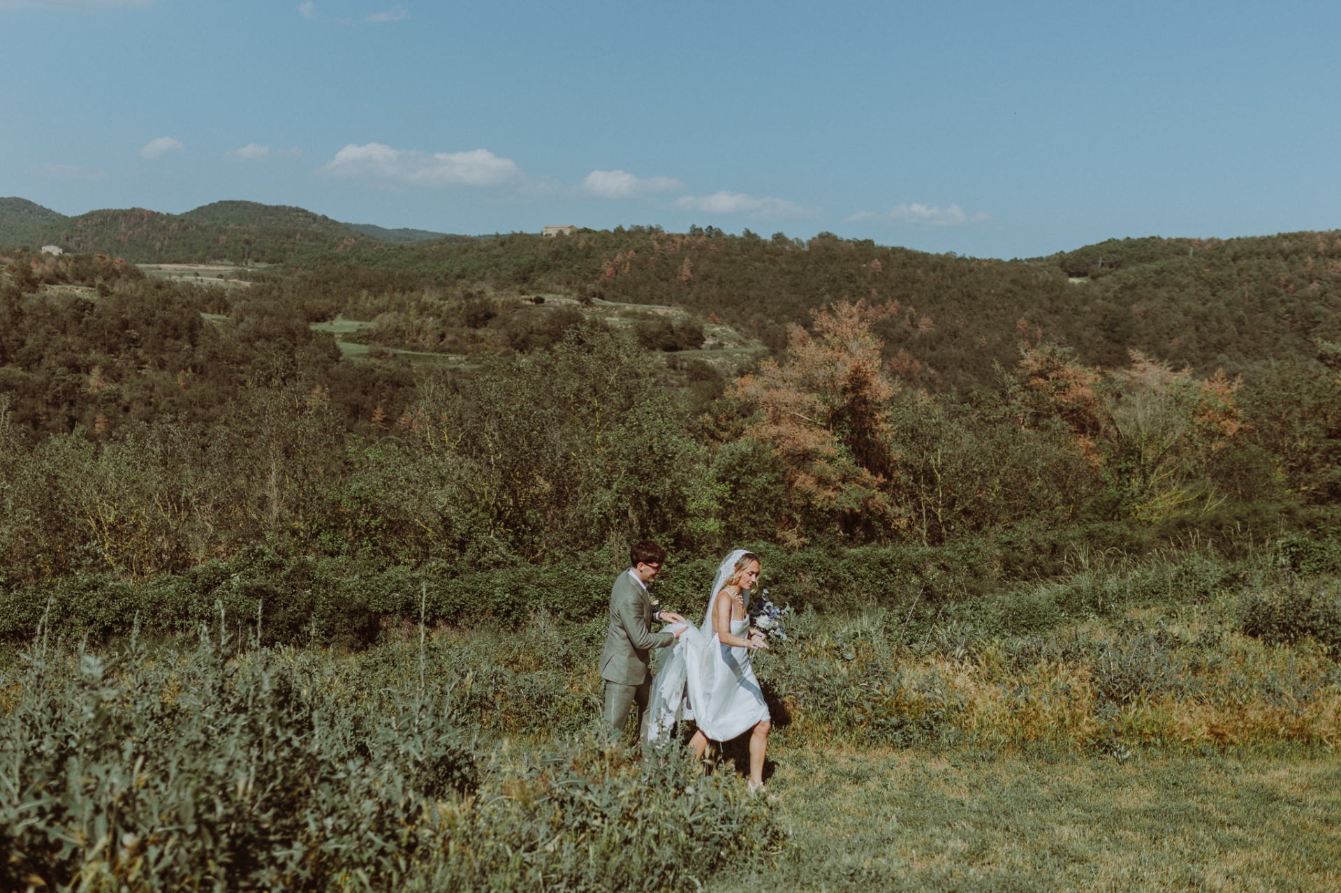 Conor helping Ellie walk through wild meadow with mountain panorama