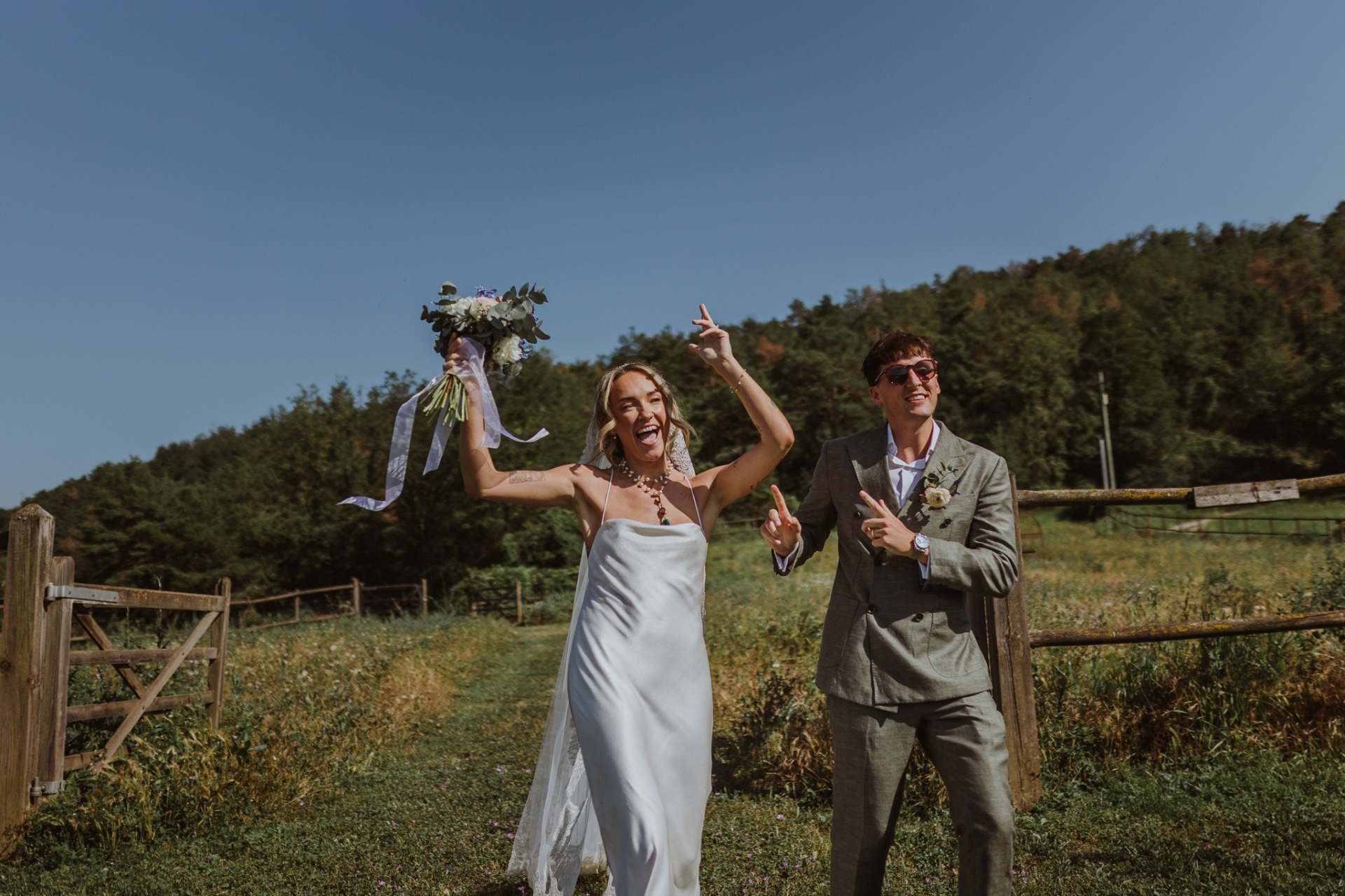 Ellie and Conor celebrating with rock and roll gestures by wooden fence