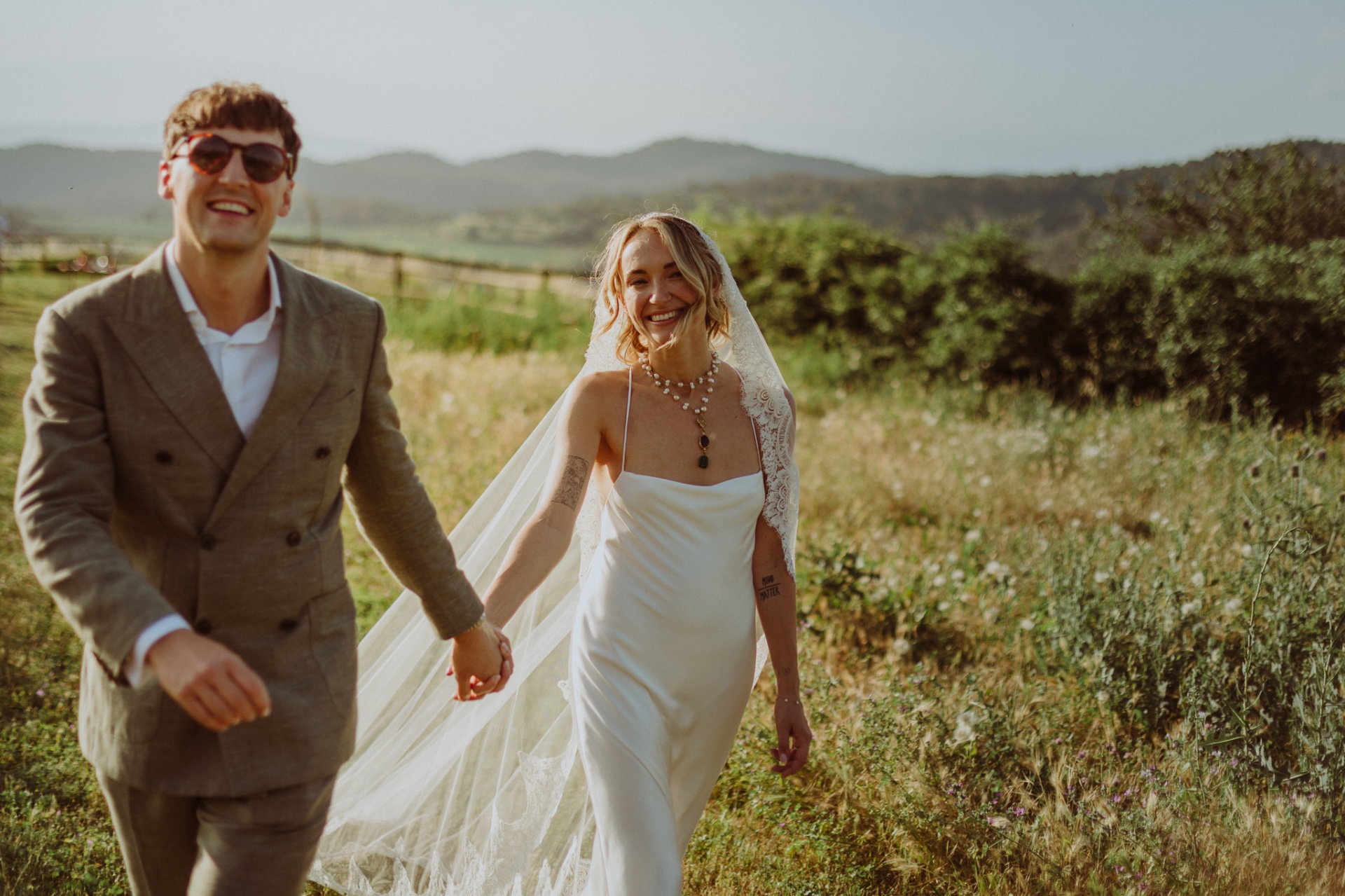 Ellie and Conor walking hand in hand through fields at golden hour