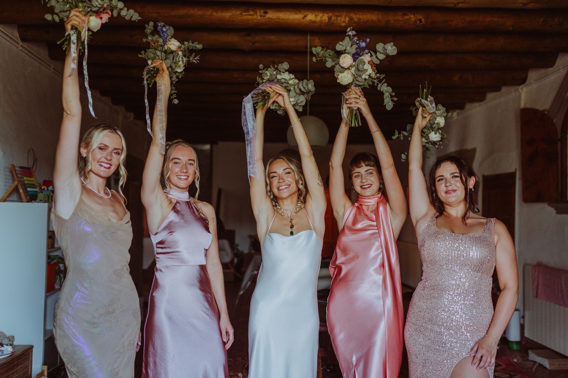 Ellie and bridesmaids raising bouquets with joy before ceremony