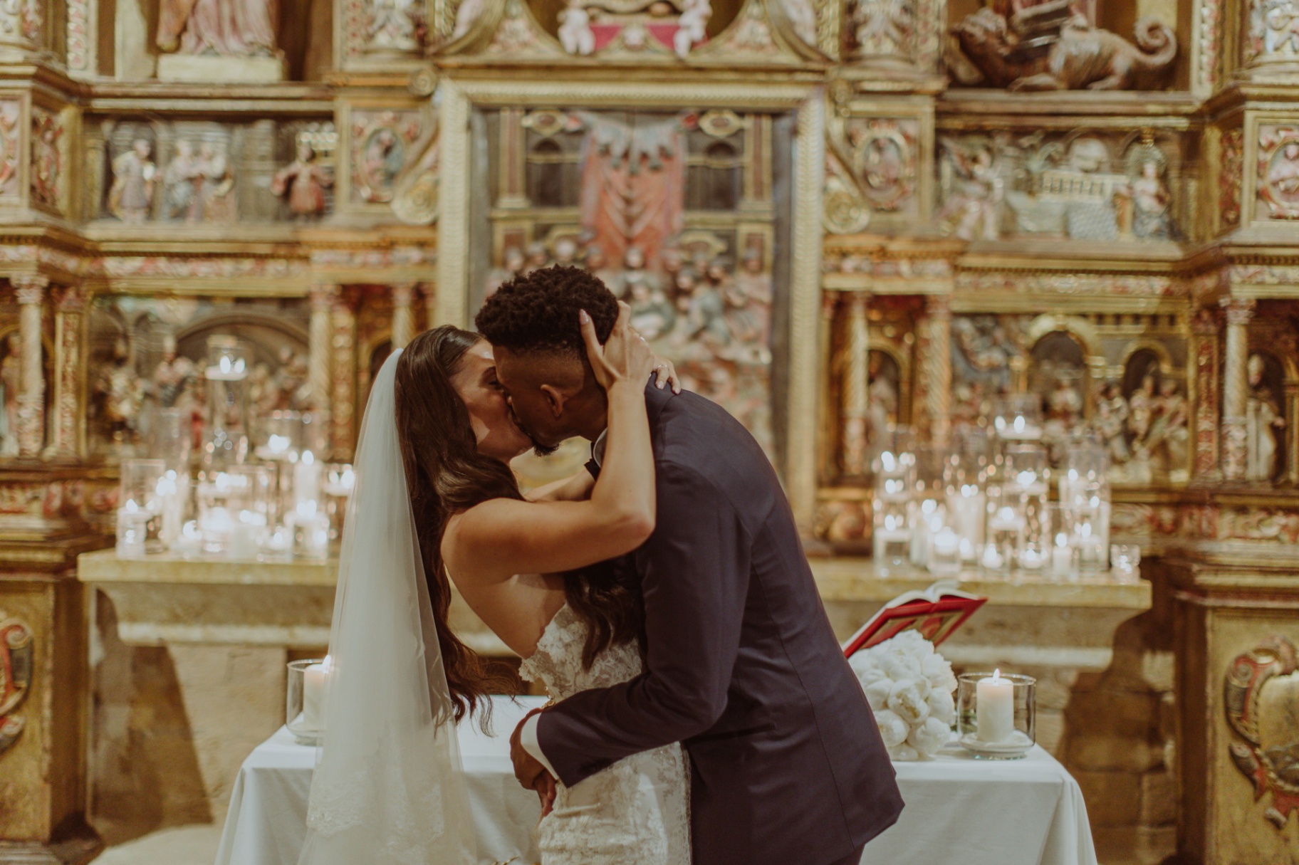 Laura and Jose passionate first kiss at ornate golden altar with candles