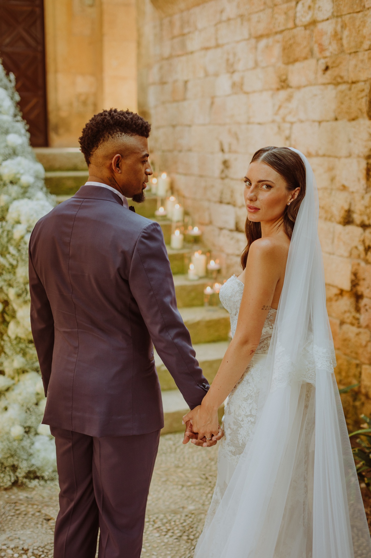 Laura looking at camera holding Jose's hand on candlelit stone steps with white flowers