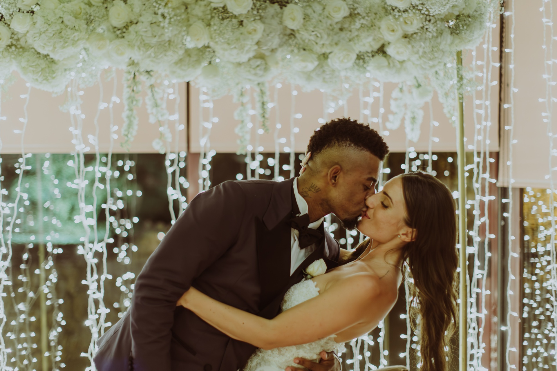 Laura and Jose kissing under white floral canopy with cascading fairy lights at Castell de Tamarit