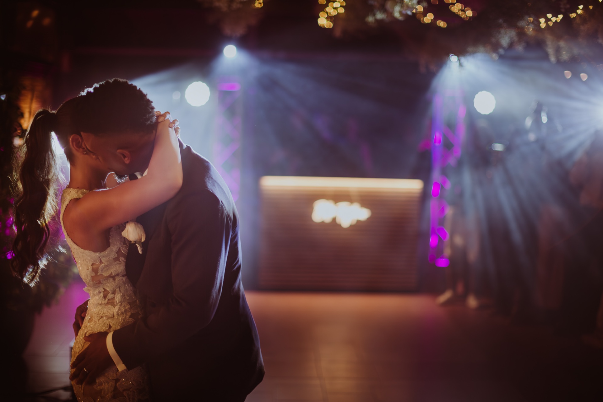 Laura and Jose embracing during first dance with purple DJ lights at reception