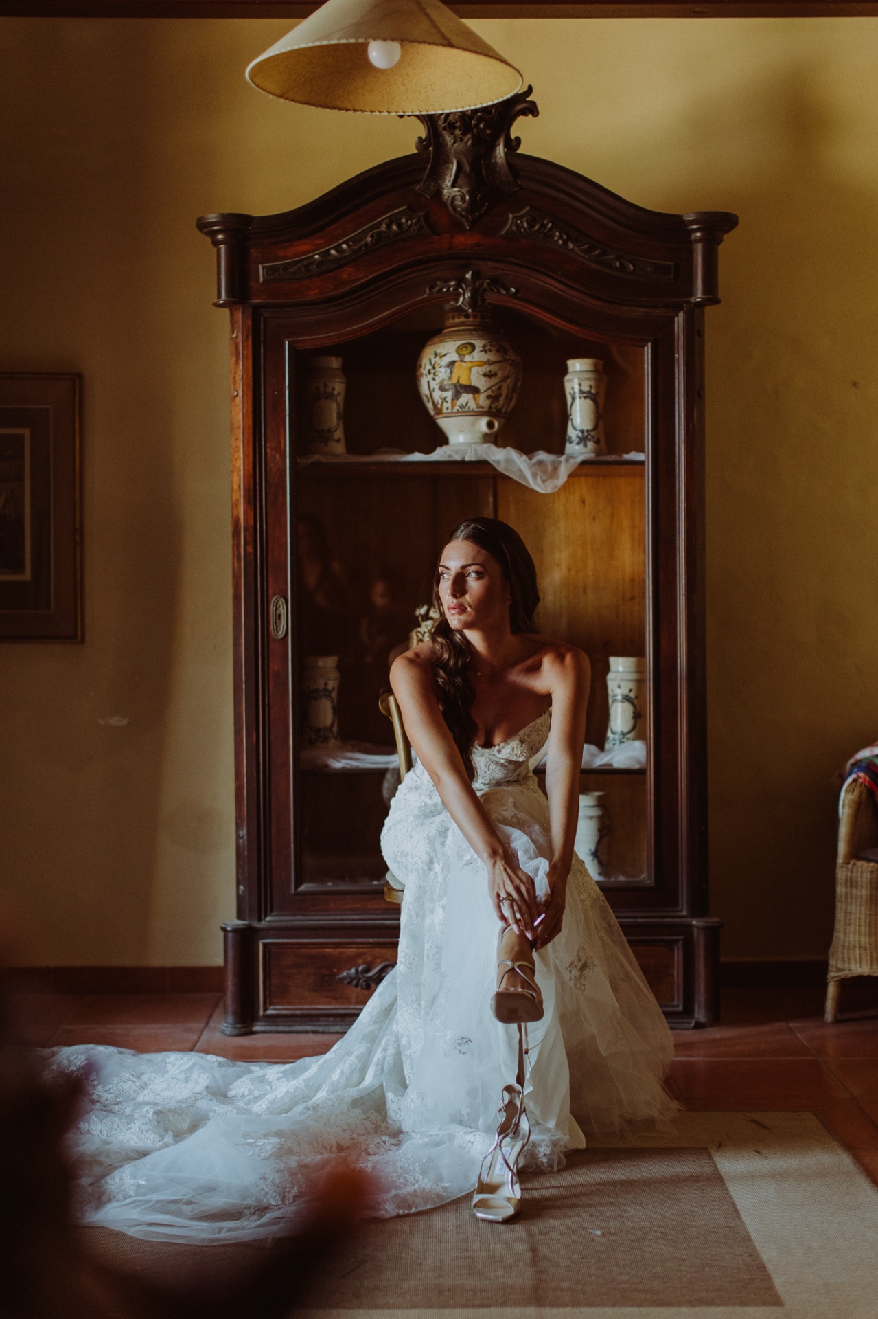 Laura seated in Ze García wedding dress with heels at antique cabinet