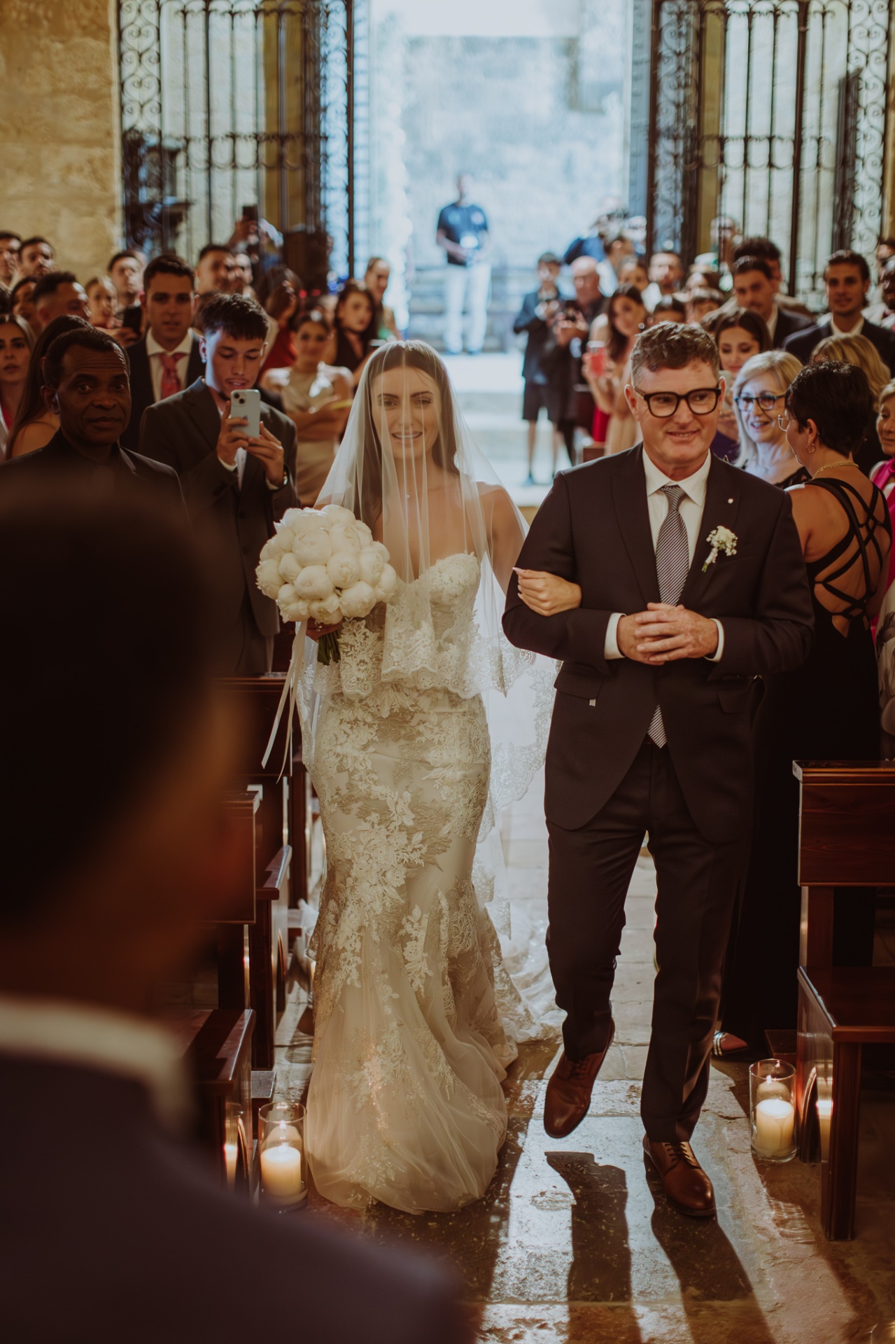 Laura walking down the aisle with her father in candlelit church ceremony