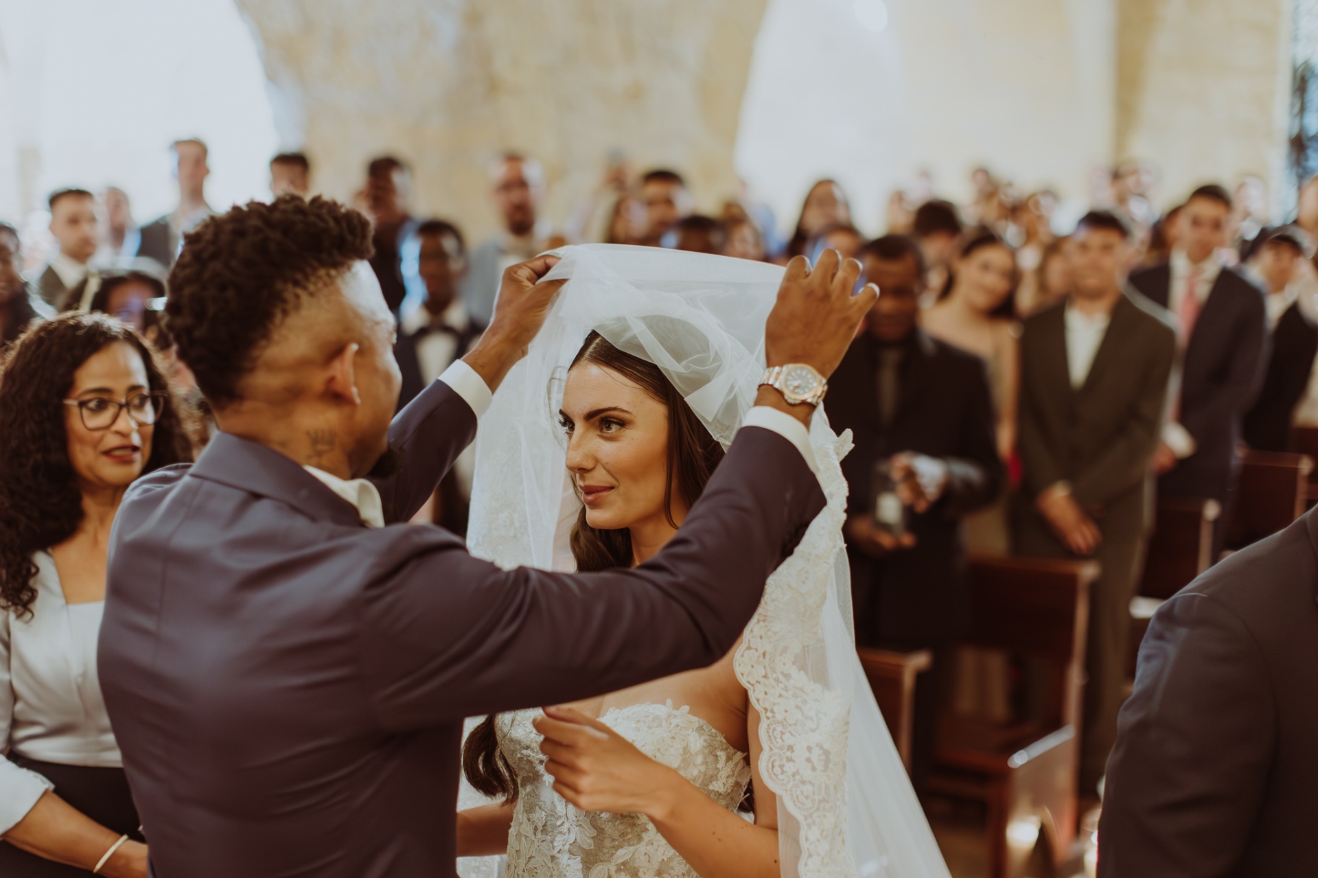 Jose lifting Laura's veil at the altar with guests watching