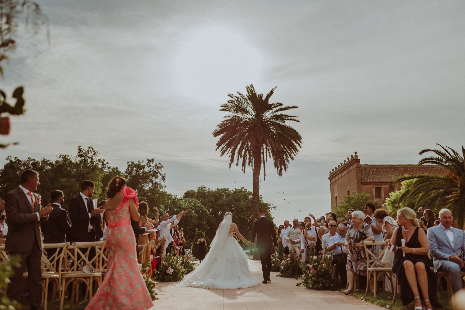 Michelle y Jorge caminando juntos por el pasillo tras la ceremonia mientras los invitados lanzan pétalos con una palmera de fondo