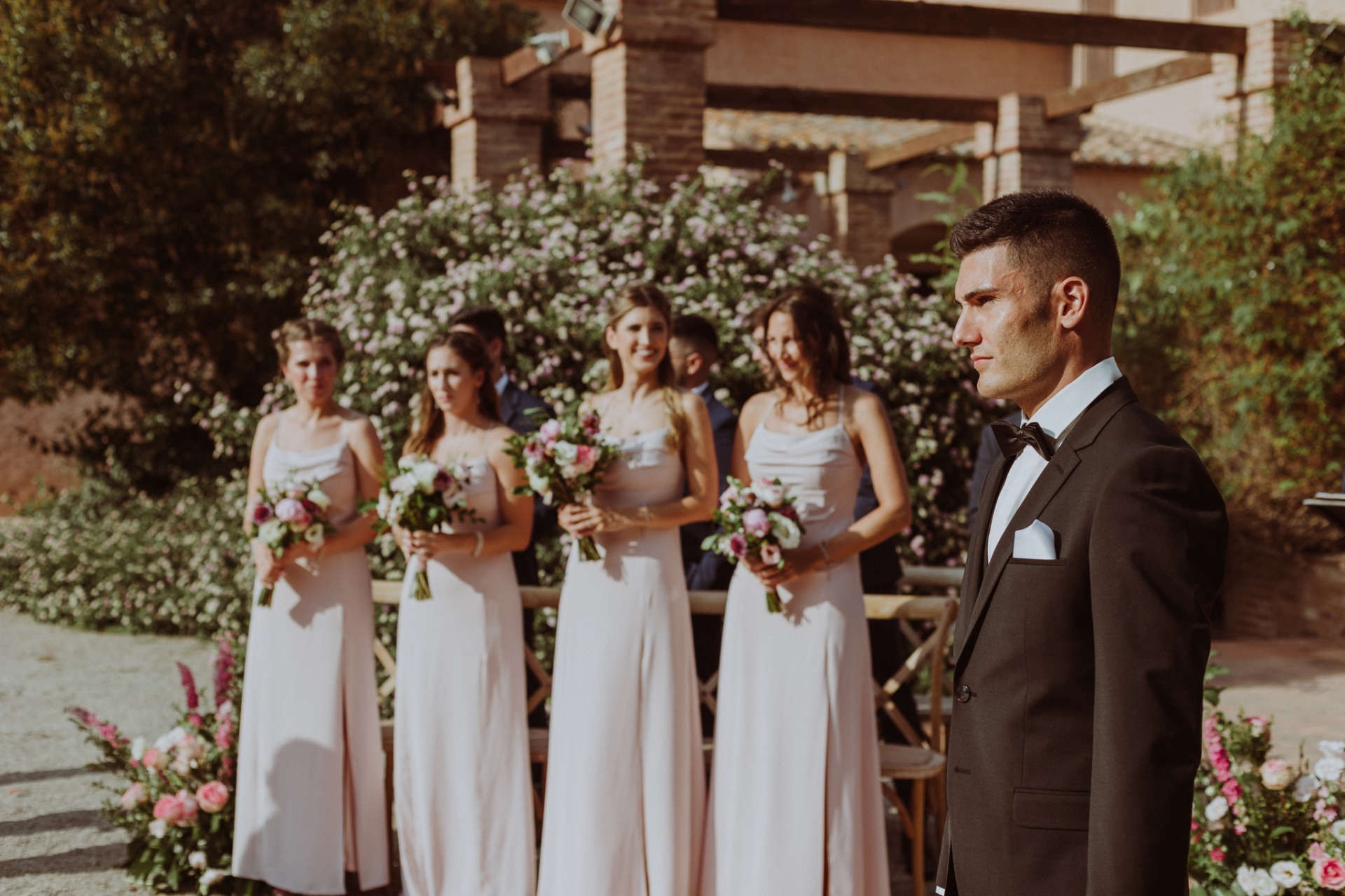 Jorge esperando emocionado en el altar con las damas de honor sosteniendo ramos de flores en los jardines de La Cartuja