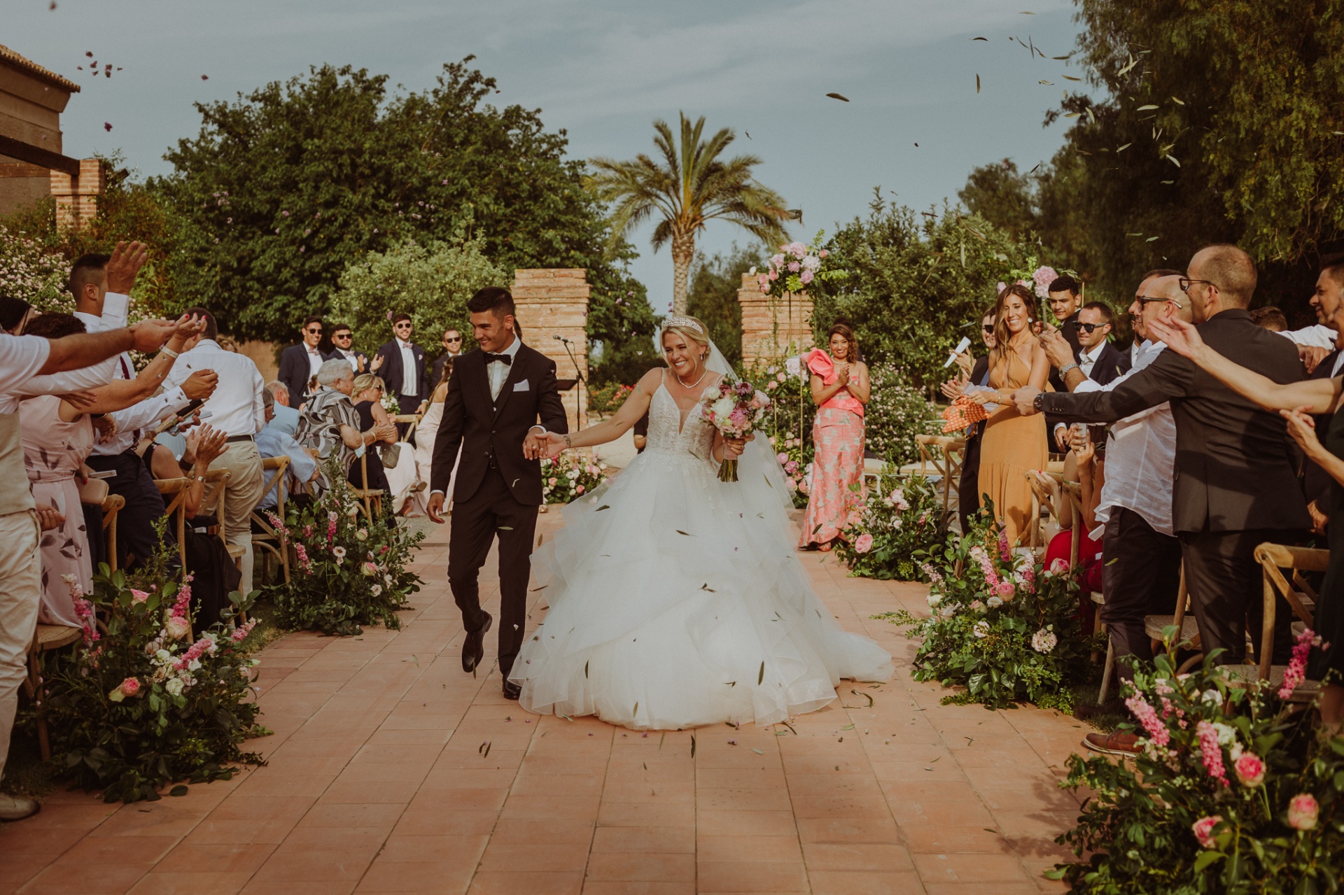 Michelle y Jorge caminando por el pasillo mientras los invitados lanzan pétalos y hojas en La Cartuja de Ara Christi