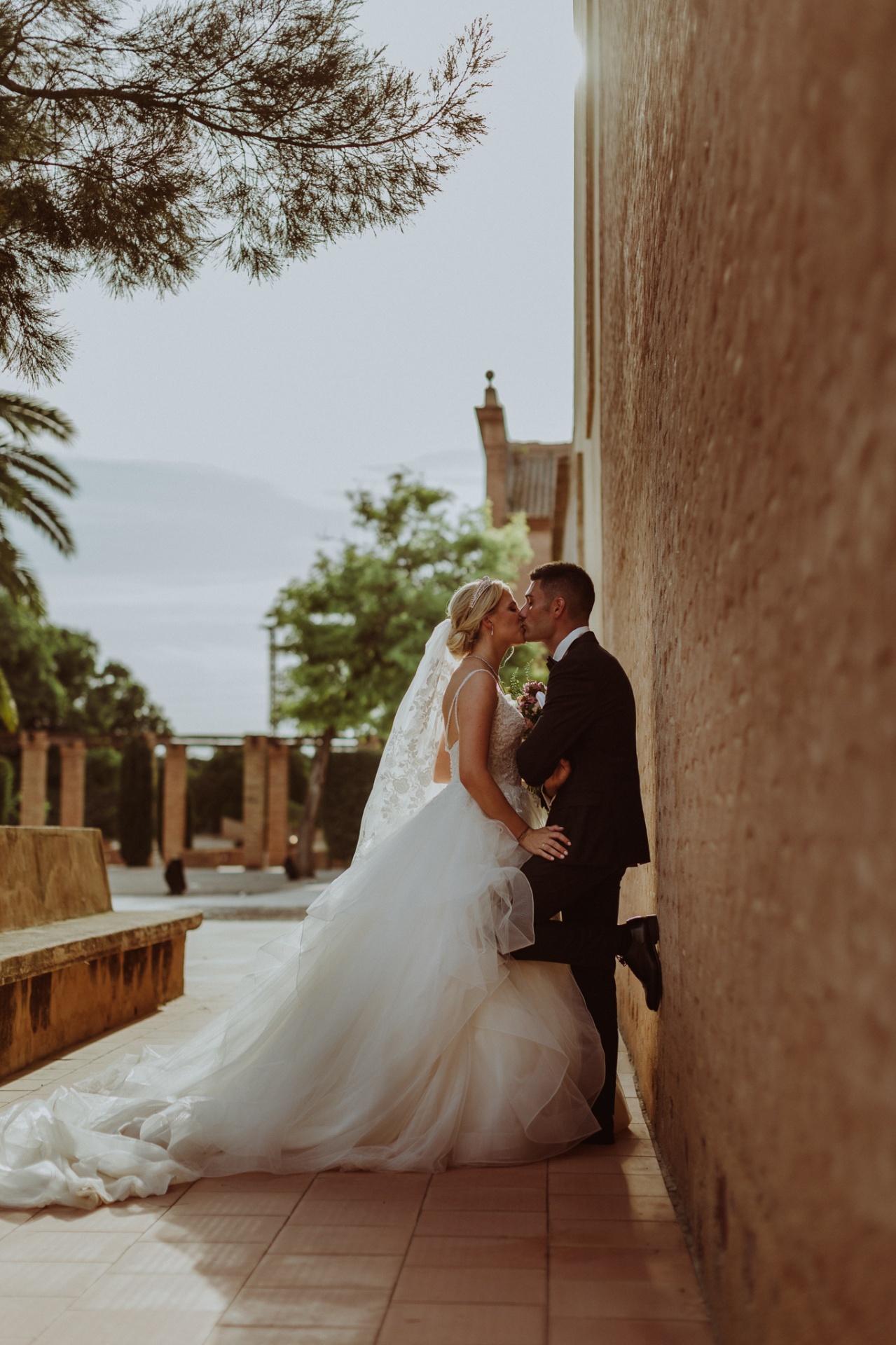Michelle y Jorge besándose en el claustro de La Cartuja de Ara Christi con luz dorada y palmeras al fondo