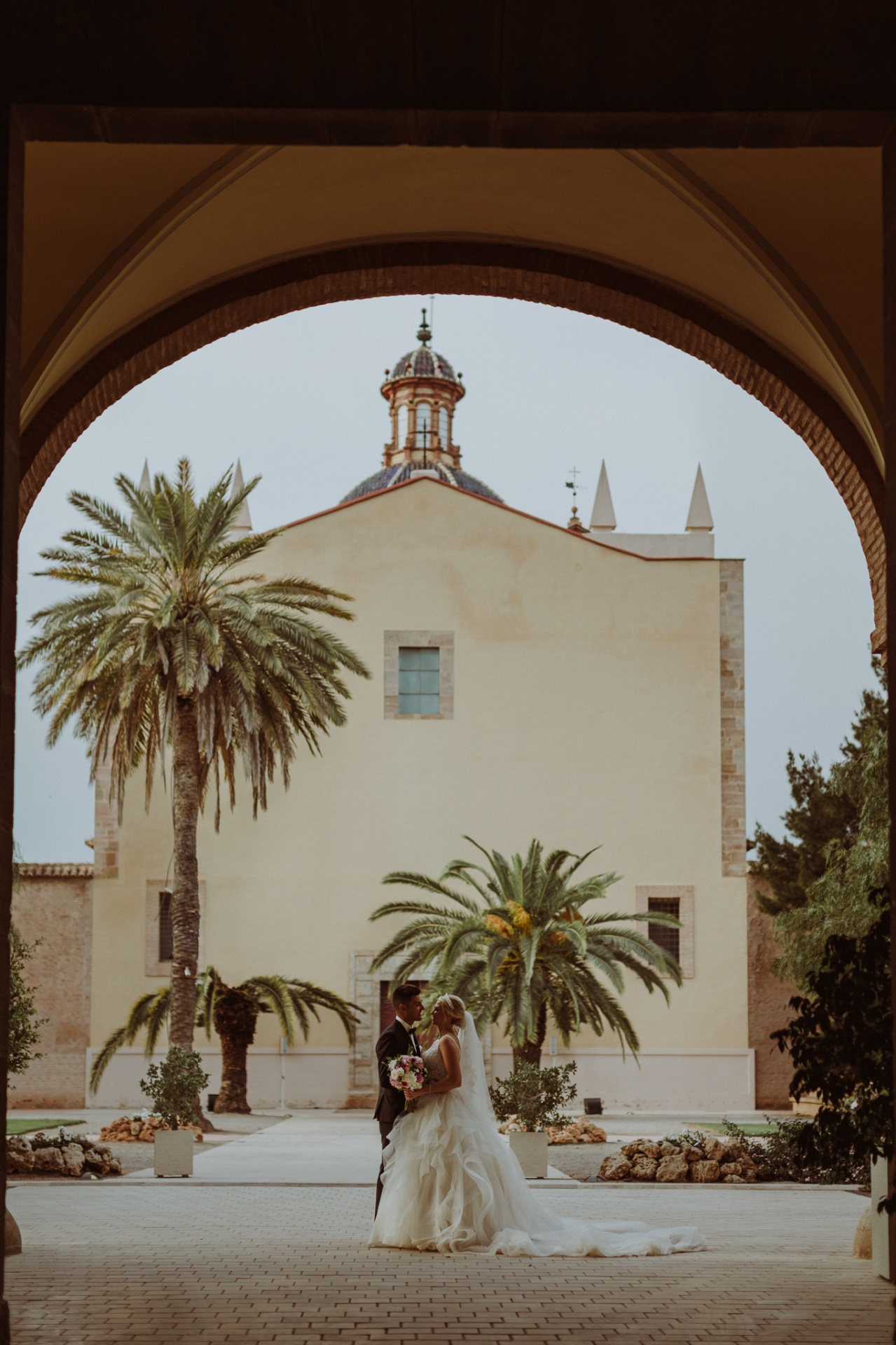 Michelle y Jorge enmarcados por el arco del claustro con la cúpula de La Cartuja y palmeras al fondo