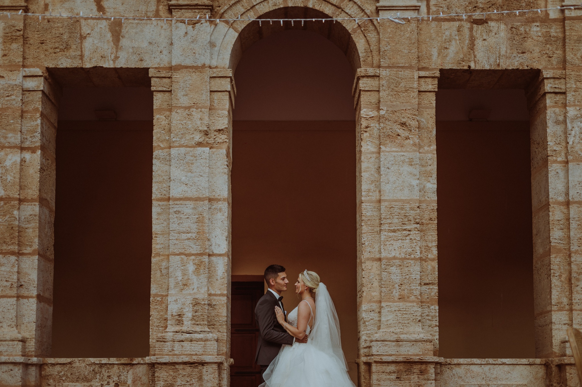 Michelle y Jorge abrazados frente a los arcos de piedra de La Cartuja de Ara Christi al atardecer