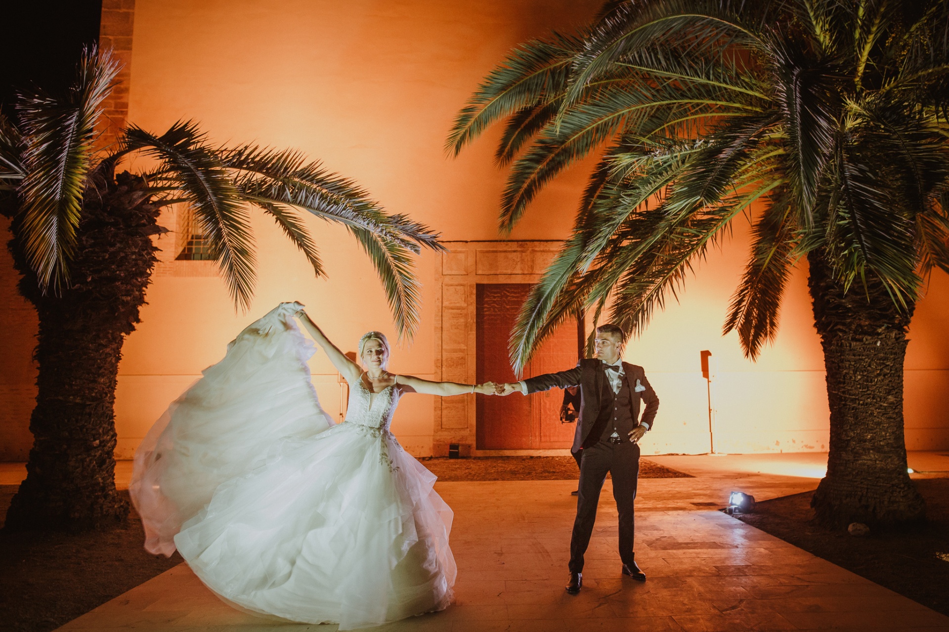 Michelle y Jorge bailando tomados de la mano bajo las palmeras iluminadas de La Cartuja de Ara Christi de noche