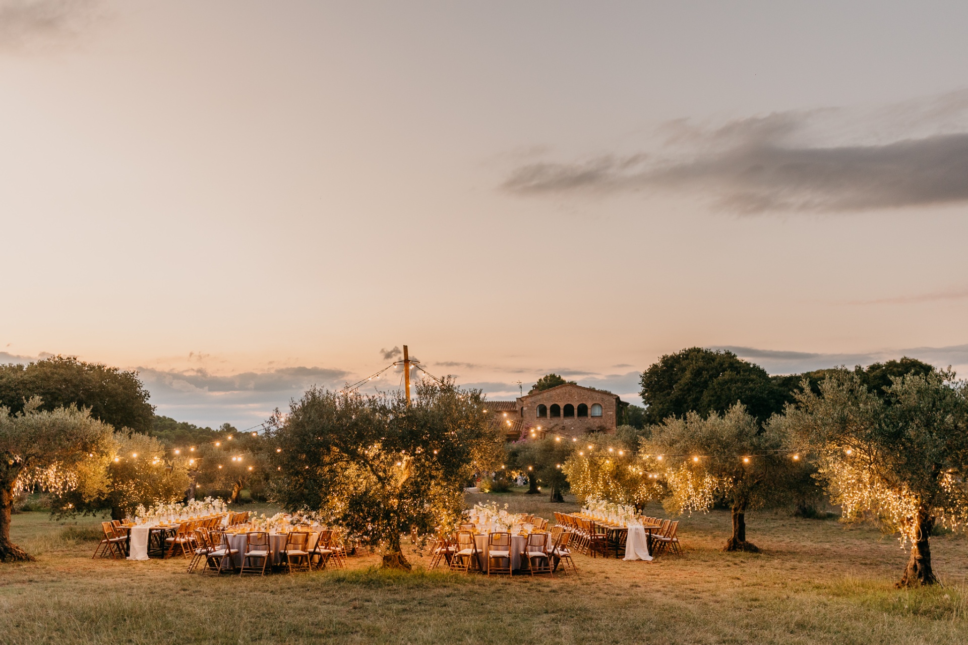 Outdoor dinner tables among olive trees with fairy lights at sunset at Mas Terrats